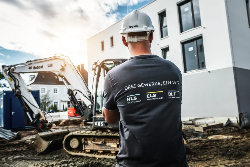 Mann mit Helm vor einem Bagger auf der Baustelle